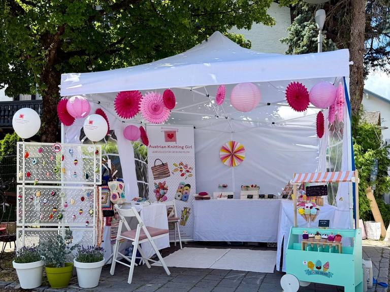 Der Marktstand von Austrian Knitting Girl auf einem Kunsthandwerksmarkt – mit rosa Lampions, Banner und gehäkelten Eistüten